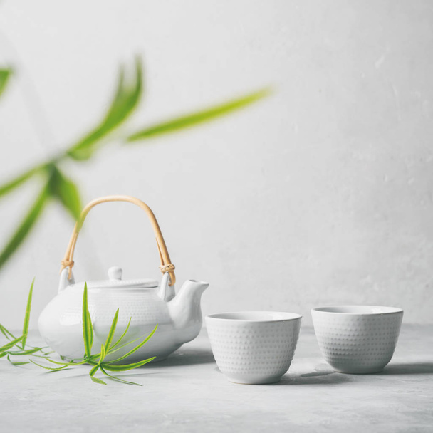Asian set with green tea, cups and teapot with bamboo leaves on grey background  - Fotografie, Obrázek