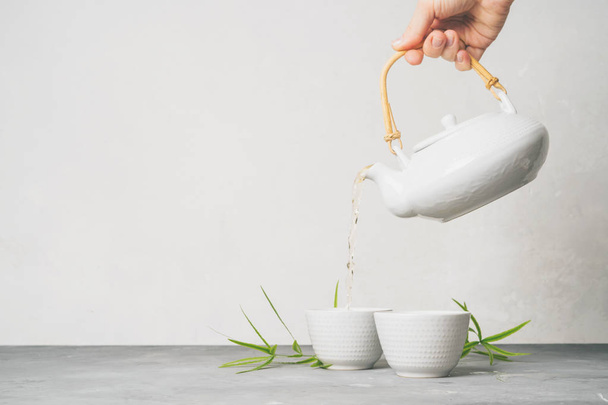 Female hand pouring green tea from a teapot into cups on white background with copy space. Asian tea set.  - 写真・画像