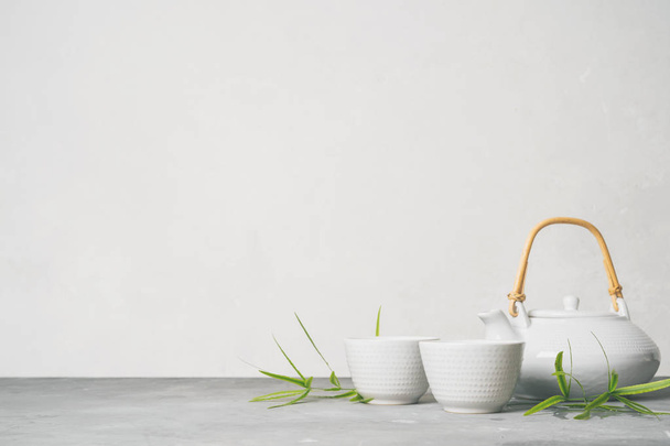Asian set with green tea, cups and teapot with bamboo leaves on grey background  - Foto, imagen