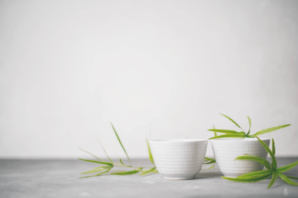 set with white porcelain tea cups with green bamboo leaves on light grey background - Valokuva, kuva
