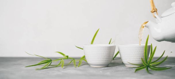 Female hand pouring green tea from a teapot into cups on white background with copy space. Long wide banne with Asian tea set.  - Foto, Bild