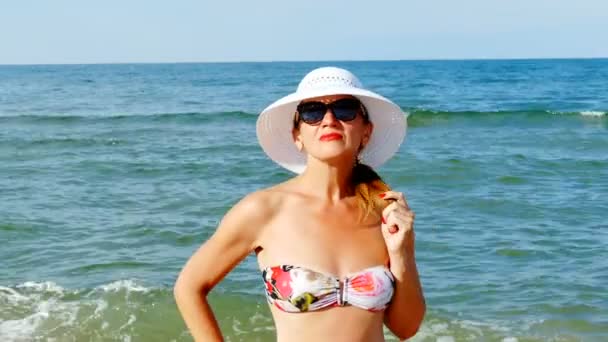    4K. Mujer con sombrero blanco y gafas, de pie cerca de las olas del océano. Tomar el sol
 - Metraje, vídeo