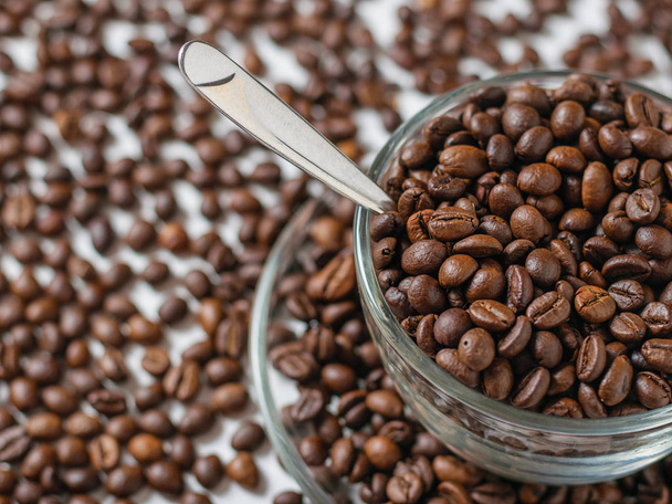 Glass bowl with coffee beans on white table background with scattered coffee beans. Grains for the preparation of the popular drink. - Fotografie, Obrázek