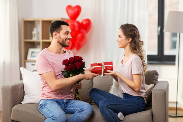 happy man giving woman flowers and present at home - Foto, Imagem