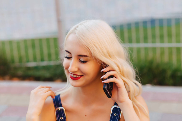 эмоциональная блондинка привлекательная девушка в солнечных очках с телефоном в теплый летний солнечный город
 - Фото, изображение