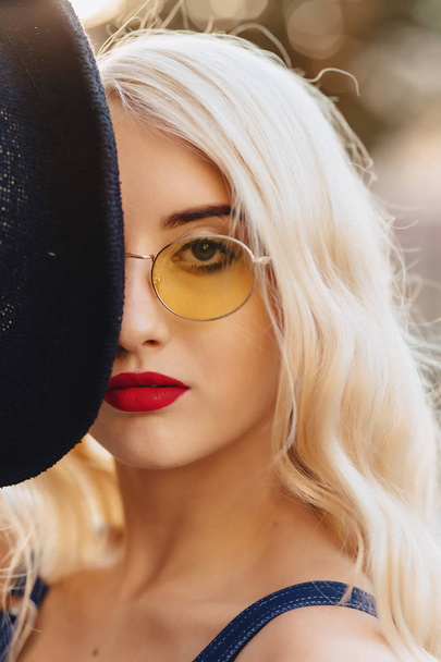 Blond aantrekkelijk meisje in zonnebrillen en stijlvolle hat op warme zomer zon stedelijke - Foto, afbeelding
