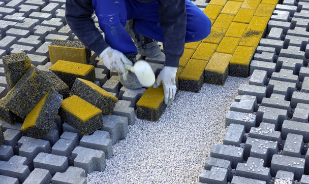 Robotnik budowlany układa blokady betonu nawierzchniowego na blachę włókniny piasku pościelowego i montażu ich na miejscu. - Zdjęcie, obraz