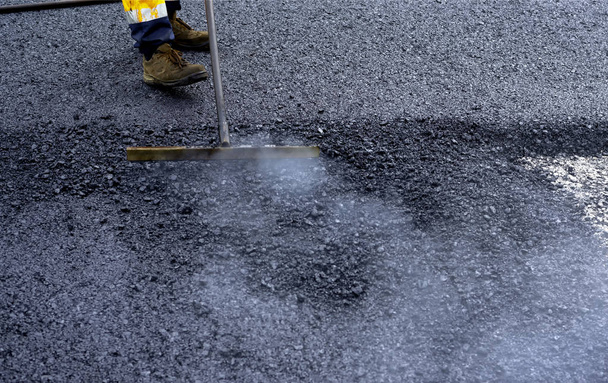 Werknemer distribueert aan de rand het asfalt aangelegd voor de aanleg van een weg - Foto, afbeelding