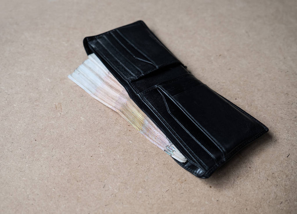 Tayland para kahverengi arka plan üzerinde siyah cüzdan dolu - Fotoğraf, Görsel