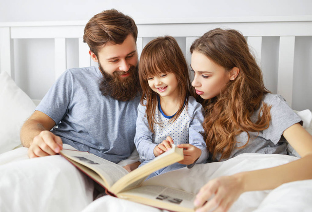 happy family mother, father and  father child daughter read a book, a fairy tale in be - Foto, afbeelding
