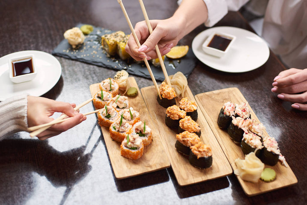 Close up female friends enjoying tasty sushi set from few rolls serving with marinated ginger and wasabi - Photo, Image