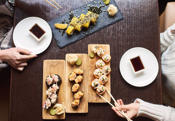vista superior de amigos comiendo en restaurante oriental, disfrutando de sushi con salsa de soja, wasabi y jengibre marinado
. - Foto, Imagen