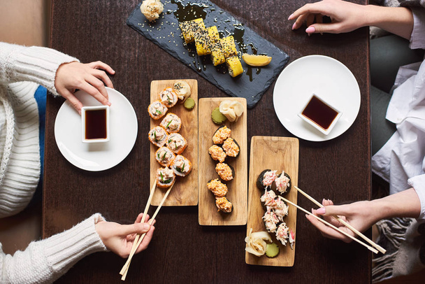 bovenaanzicht van vrienden eet in Oosterse restaurant genieten van sushi set met gemarineerde gember, soja saus en wasabi. - Foto, afbeelding