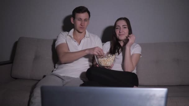 Glückliches Paar schaut sich einen Film im Fernsehen an und sitzt zu Hause auf einer Couch - Filmmaterial, Video