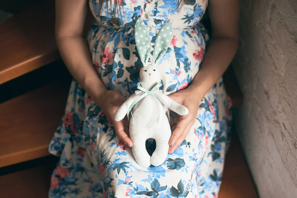 a terhes anya virágos ruha gazdaság aranyos játék bunny a jövőben gyermek közelről - Fotó, kép