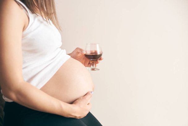 Вид сбоку беременной женщины с большим животом, сидящей дома и пьющей красное вино
 - Фото, изображение