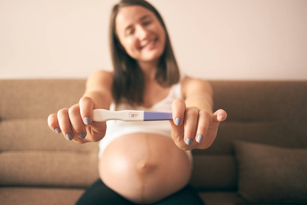 Selektiver Fokus des Schwangerschaftstests in den Händen einer lächelnden Frau im weißen Hemd - Foto, Bild