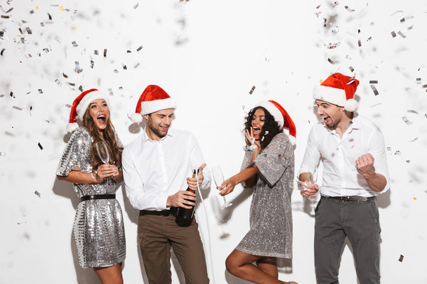 Ομάδα φίλων τέσσερις χαρούμενα ντυμένοι κομψά στέκεται απομονωθεί σε λευκό φόντο, γιορτάζει το νέο έτος, να πίνουν σαμπάνια - Φωτογραφία, εικόνα