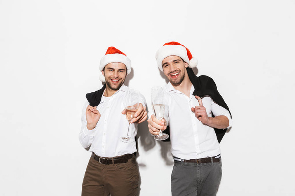 Two cheerful smartly dressed men standing isolated over white background, celebrating New Year, drinking champagne - Fotografie, Obrázek