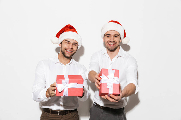 Two cheerful smartly dressed men standing isolated over white background, celebrating New Year, holding present boxes - Photo, Image