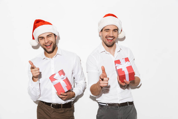 Two cheerful smartly dressed men standing isolated over white background, celebrating New Year, holding present boxes - Zdjęcie, obraz