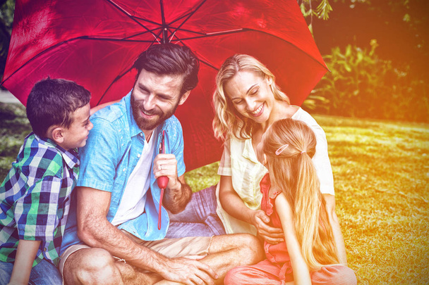 Happy family with umbrella sitting on grass at yard - Foto, Bild