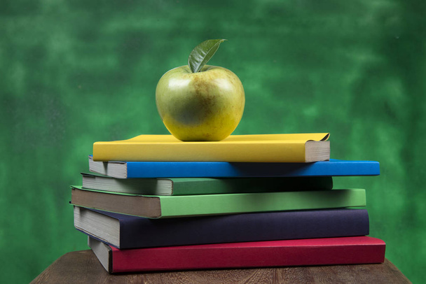 grüne Apfelfrüchte auf einem Bücherstapel, auf der Rückseite von Schulklassen - Foto, Bild