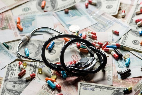 close up of colorful pills and stethoscope on cash background - Foto, afbeelding