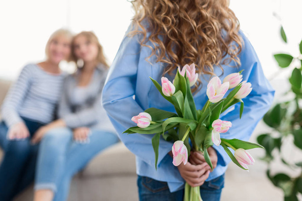 Cute teenage girl hiding flowers for her granny and mother - Foto, immagini