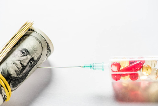 Закрыть шприц с лекарствами рядом с рулоном денег на белом фоне
  - Фото, изображение