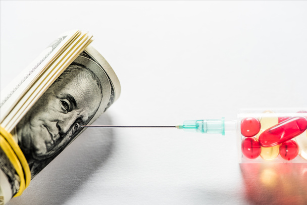 fechar a seringa com pílulas perto do rolo de dinheiro no fundo branco
  - Foto, Imagem