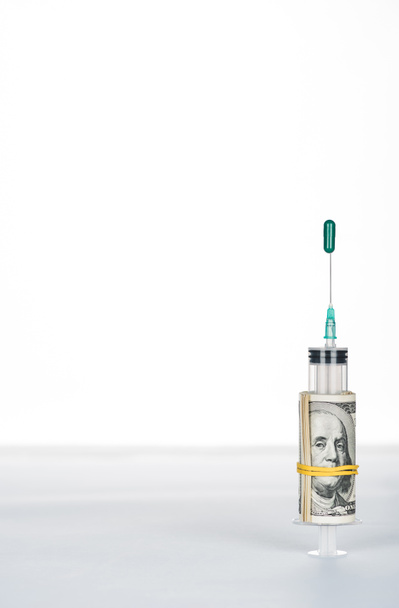 Geldrolle und Spritze mit grüner ovaler Pille auf Nadel isoliert auf weißer - Foto, Bild