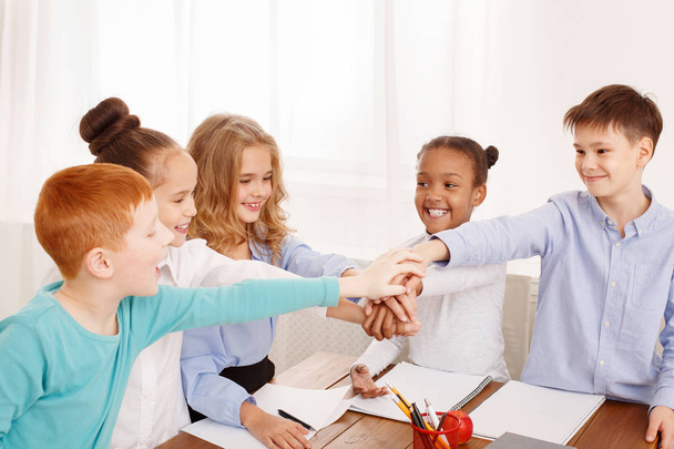 Children putting their hands together in classroom - Valokuva, kuva
