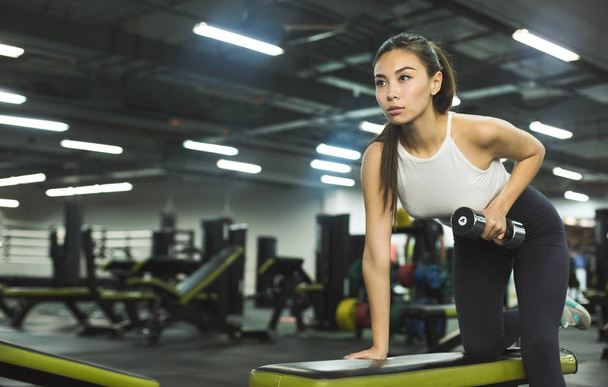 Schlankes Mädchen wärmt sich im Fitnessstudio mit Gewichten auf - Foto, Bild