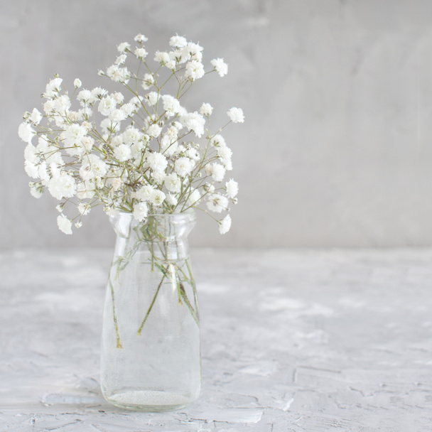 Ramo de pequeñas flores blancas en un frasco sobre un fondo gris
 - Foto, Imagen