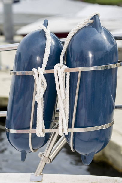Dois pára-lamas azuis em um retrato com cordas brancas em um suporte em um corrimão de barco
 - Foto, Imagem