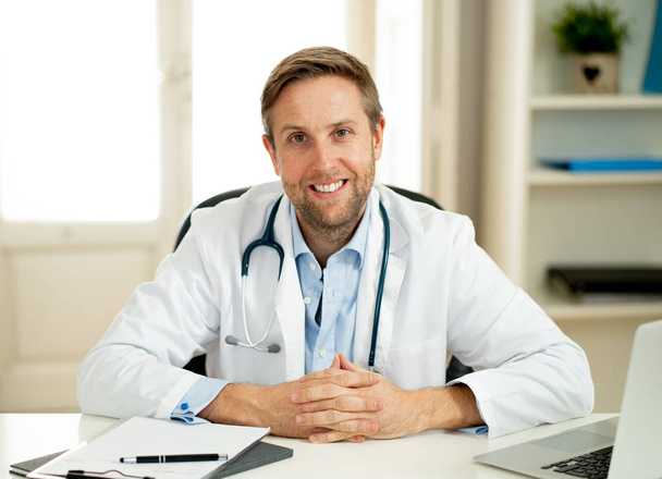 Portrait of happy caucasian doctor in white coat working on laptop computer and paperwork in clinic hospital desk for Health care successful professionals and Medical insurance advertisement. - 写真・画像