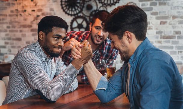 Male friends arm wrestling each other in bar - Photo, Image