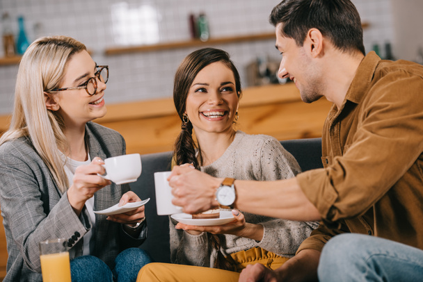 fröhliche Freunde plaudern während sie Tassen im Café halten - Foto, Bild