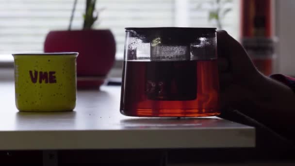 Mans hand holding glass teapot with hot tea pours it into big mug. - Footage, Video