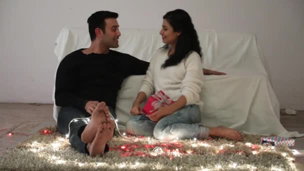 A beautiful happy young couple sitting on the floor and exchanging gift - Filmagem, Vídeo
