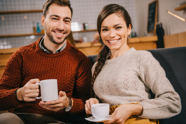 couple holding cups and smiling in cafe - Photo, Image