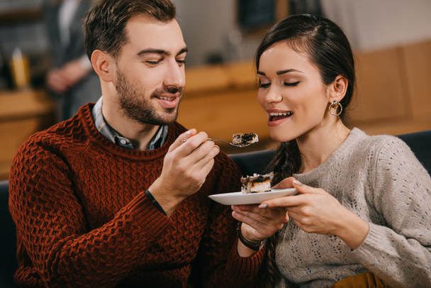 handsome man feeding attractive woman with cake in cafe - Zdjęcie, obraz
