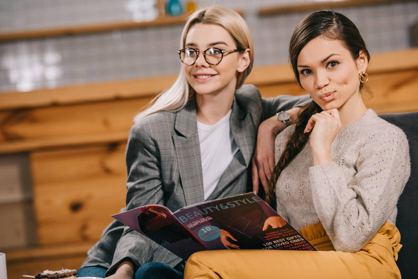 attractive woman holding beauty magazine and sitting with friend - Foto, Bild