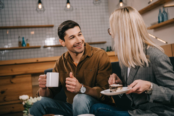 smiling man looking at girlfriend with cake in cafe - Foto, Imagem
