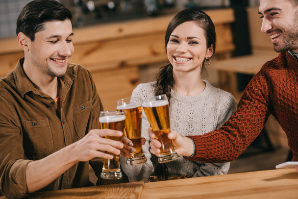 happy woman smiling near friends while clinking with beer  - Photo, Image