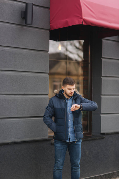 Handsome man in a jacket look at the watch and standing on the street - Photo, Image