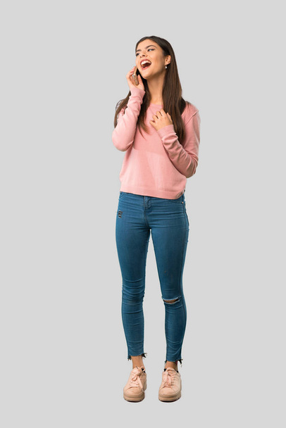 Повне тіло дівчини-підлітка з рожевою сорочкою, що веде розмову з мобільним телефоном на ізольованому сірому фоні
 - Фото, зображення