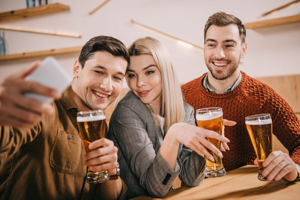 smiling man taking selfie with friends holding glasses of beer - 写真・画像