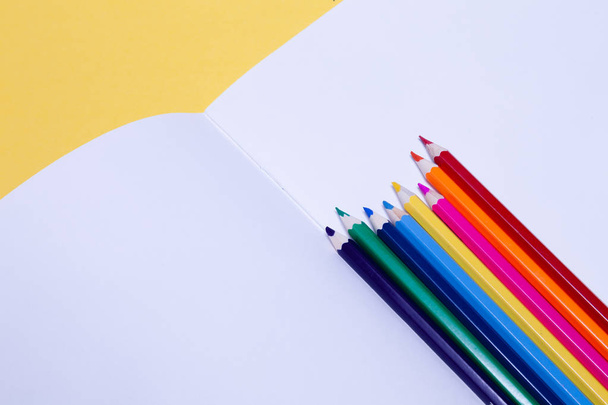 Seamless colored rainbow pencils on sheets of white paper school drawing album on yellow  background isolated.   Concept of free space, copyspace, cover of notebook use for professional drawin - 写真・画像